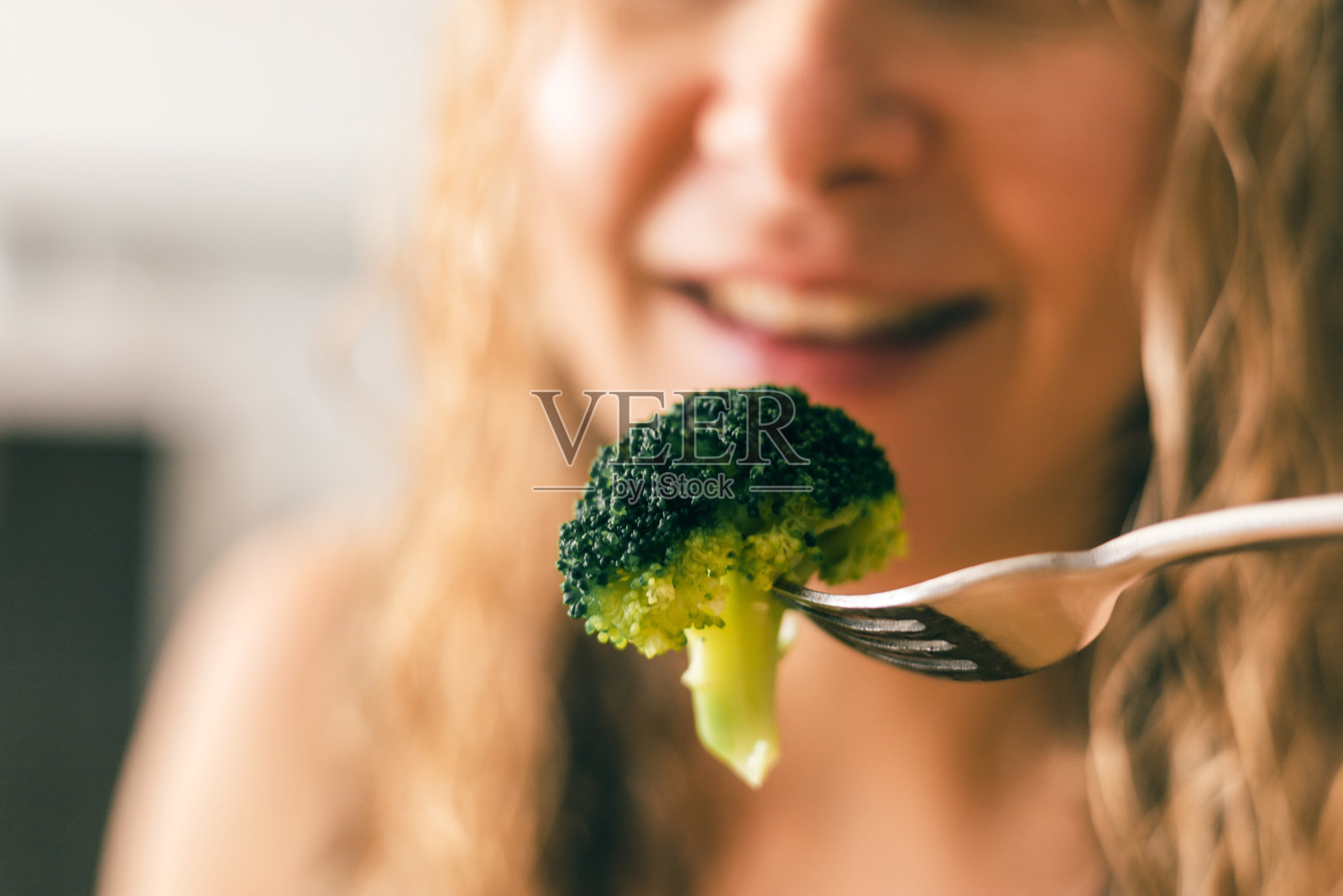 一位女士在享受健康饮食生活方式的时刻,叉子上放着新鲜煮熟的西兰花照片摄影图片