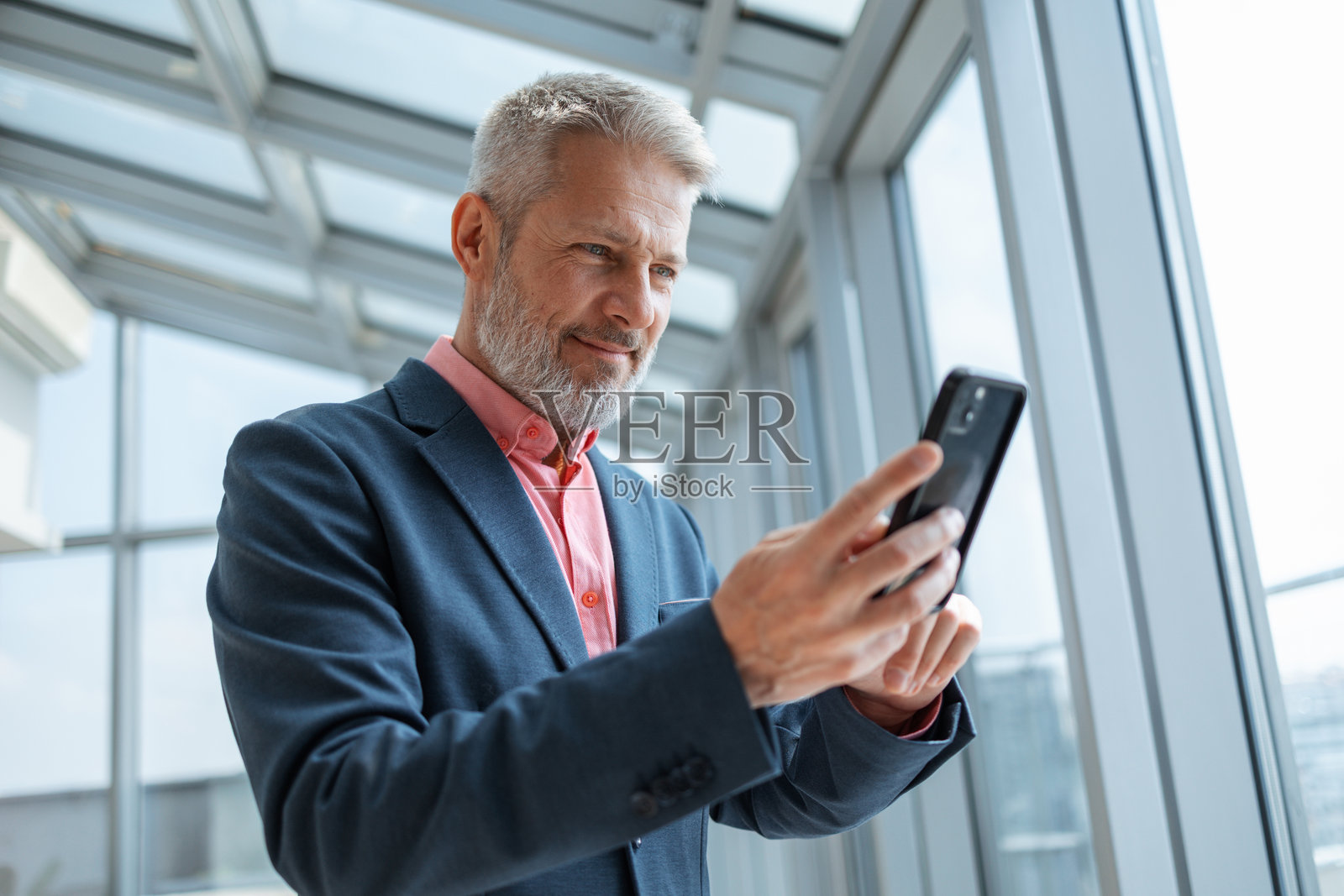 专业的男士在明亮现代的办公室环境中,使用智能手机照片摄影图片