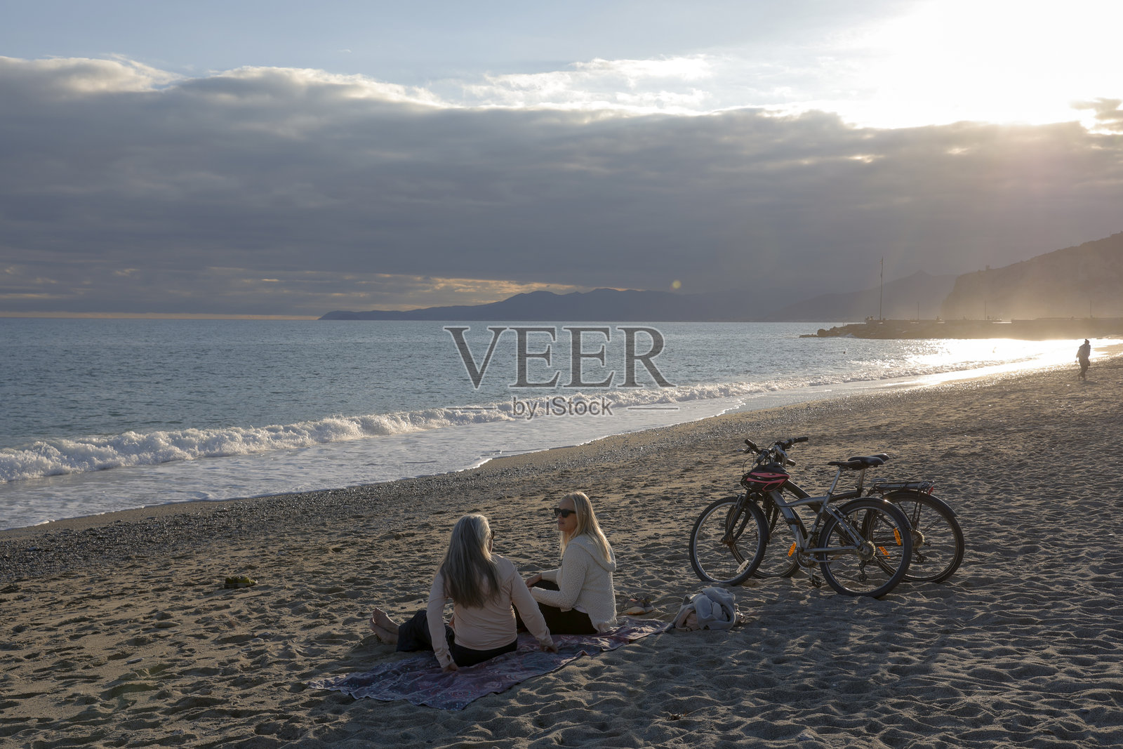 夕阳下,成熟的女性在海滩上骑着自行车聊天照片摄影图片