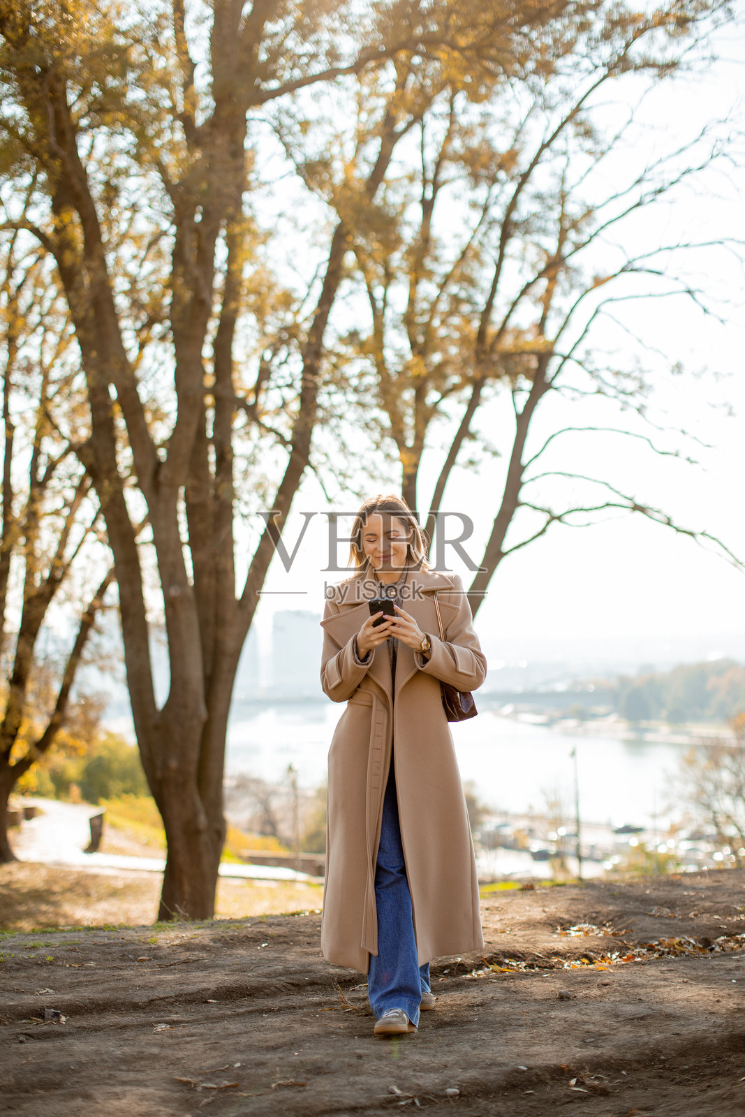 一位身穿长款外套的女士在秋季的公园里悠闲漫步照片摄影图片