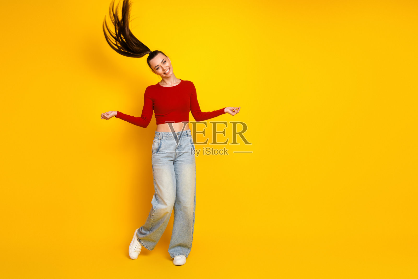 年轻女子身穿红色露脐上衣和牛仔裤,在明亮的黄色背景前载歌载舞,笑容灿烂照片摄影图片