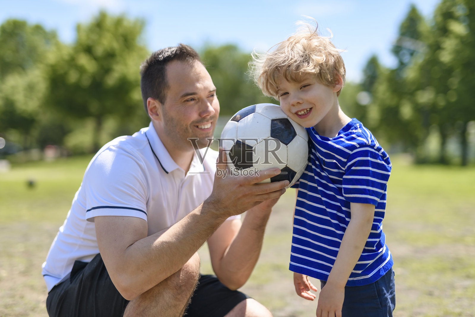 年轻的父亲和他的小儿子在足球场上踢足球照片摄影图片