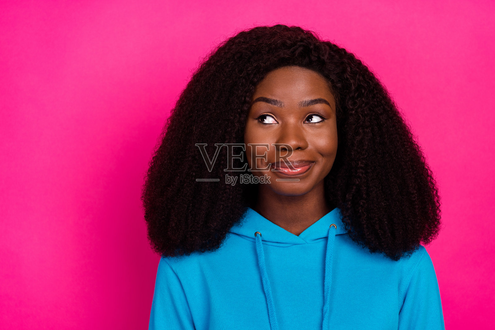 穿着蓝色卫衣的迷人女人,眼神空洞地望向远方,背景是明亮的粉红色,照片肖像照片摄影图片