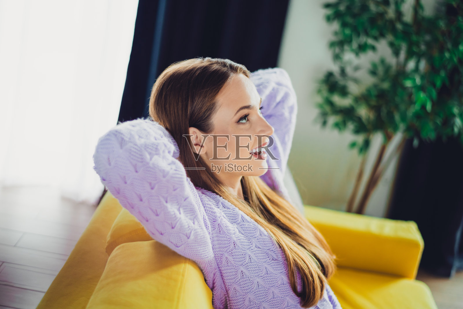 穿着薰衣草色毛衣的年轻女子,在舒适客厅的亮黄色沙发上放松,享受居家舒适照片摄影图片