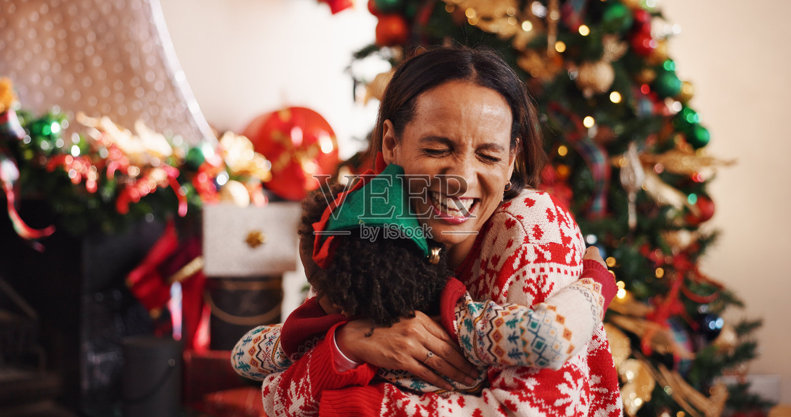 快乐的妈妈拥抱孩子,充满爱意地庆祝圣诞节、节日或新年,一家人在家中团聚。微笑的母亲和孩子,相拥或关怀,共度节日周末,享受家庭时光或亲子之情。照片摄影图片