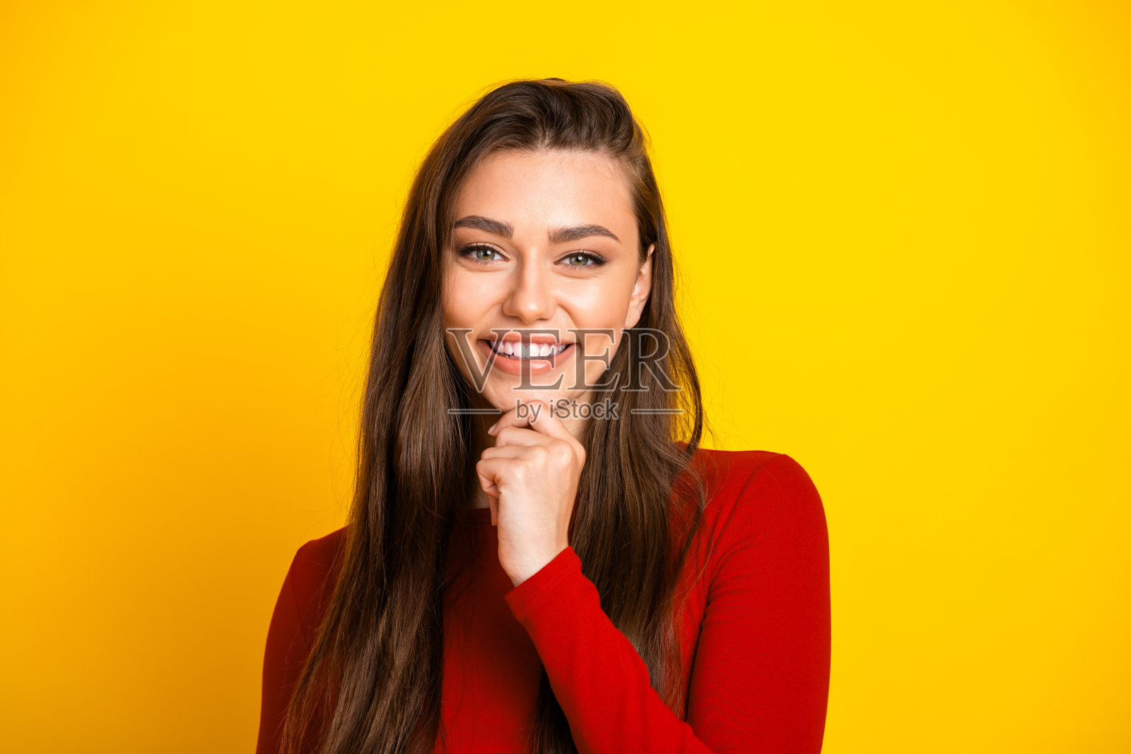 年轻女子,留着棕色长发,身穿红色上衣,在明亮的黄色背景前温暖地微笑,用于时尚生活方式广告宣传照照片摄影图片