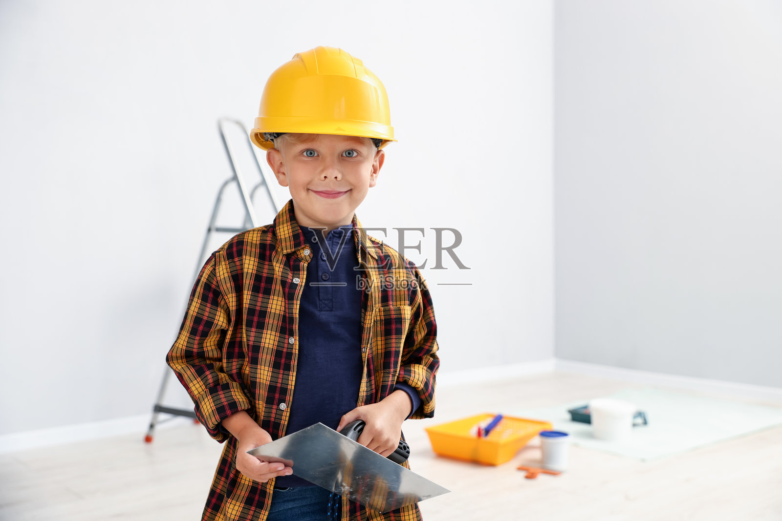 职业选择。小男孩拿着抹刀,在室内假装自己是建筑工人,有文字空间照片摄影图片