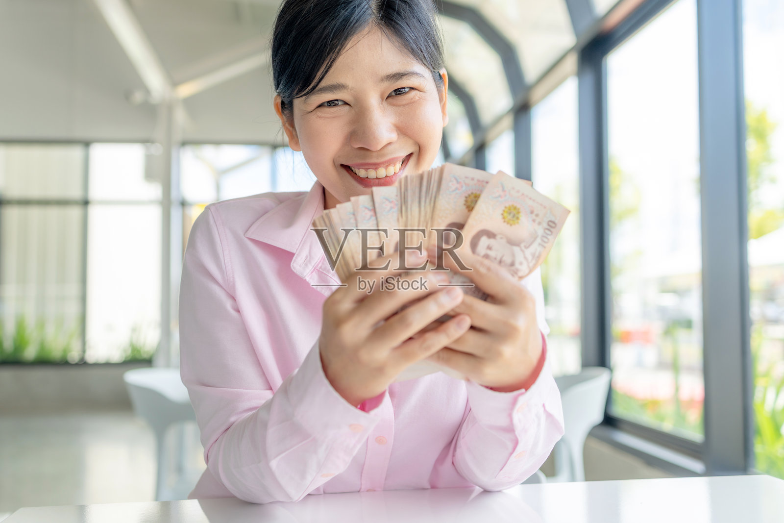 钱,现金,财富,一位快乐的亚洲女性手持泰铢纸币,展示财富、成功和财务幸福,特写照片摄影图片