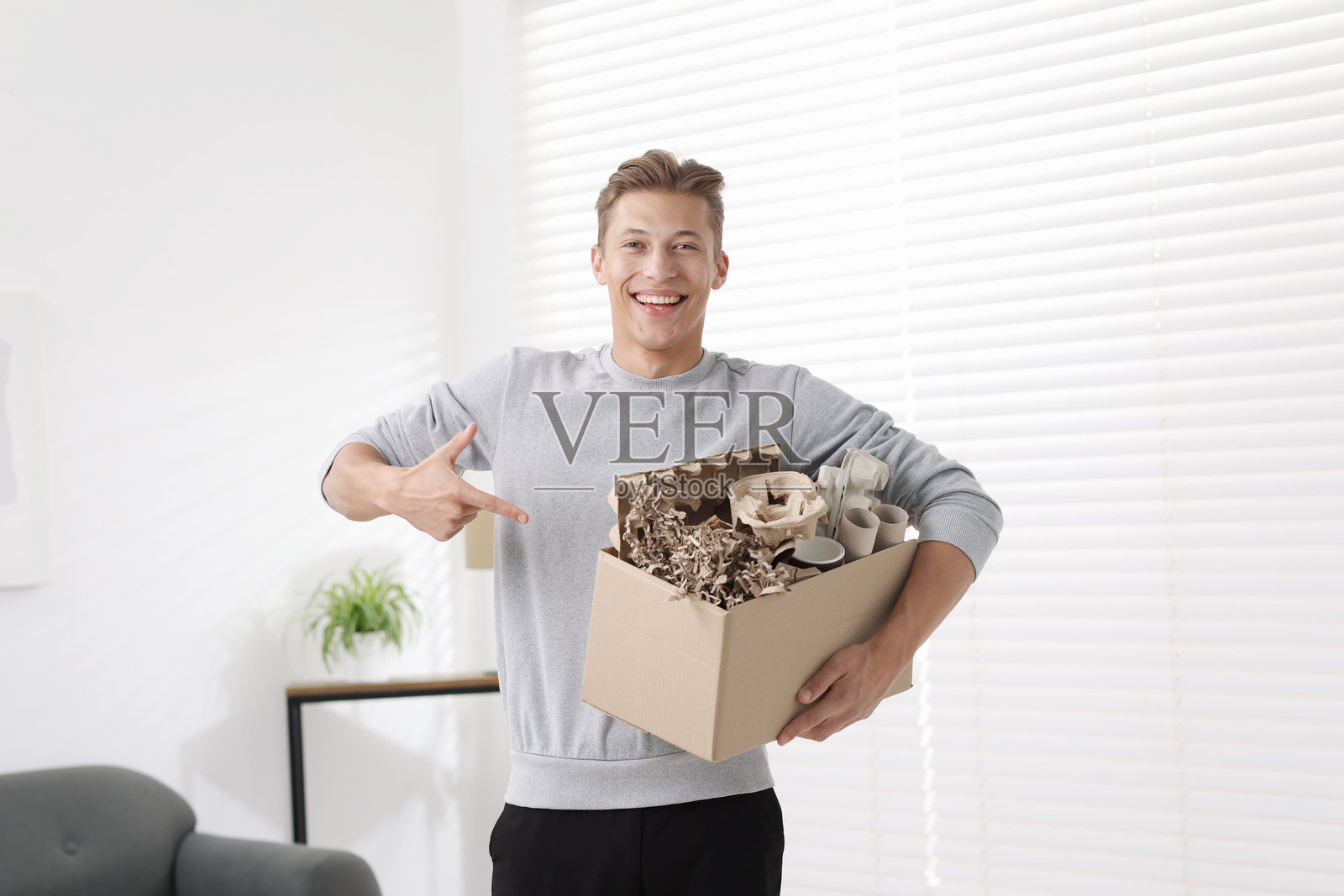 回收。室内,一位面带微笑的男士正拿着一个装有不同废纸的纸板箱照片摄影图片