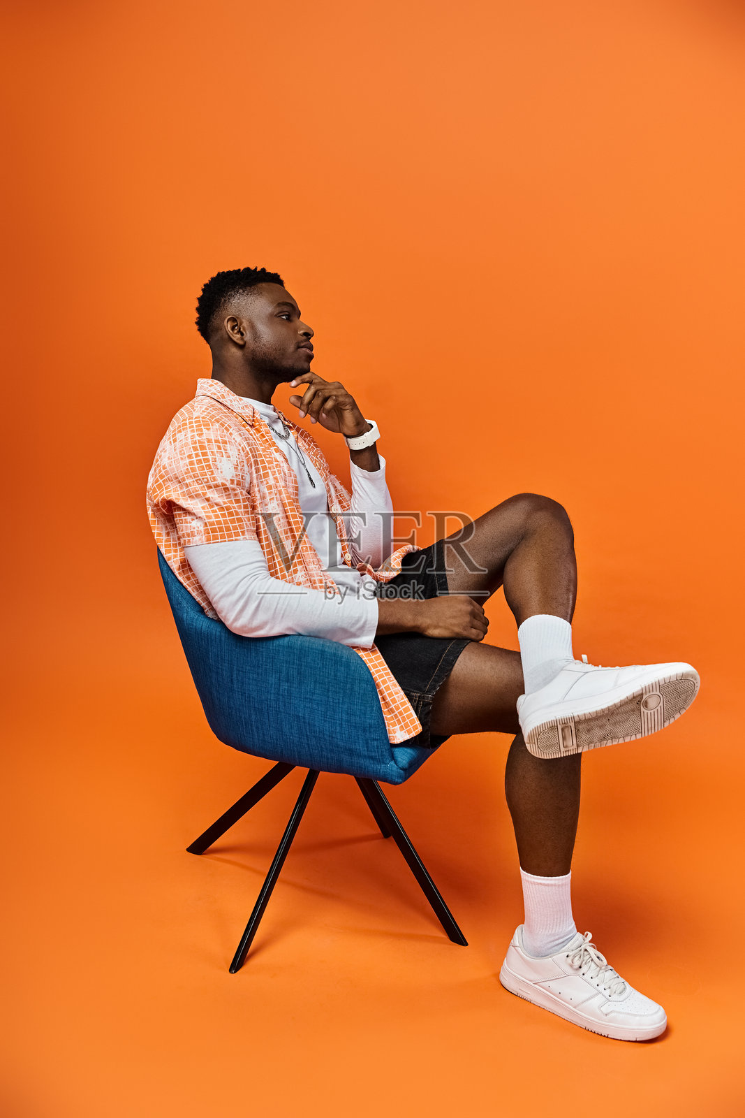 时髦的年轻男子坐在椅子上,背景是鲜艳的橙色照片摄影图片