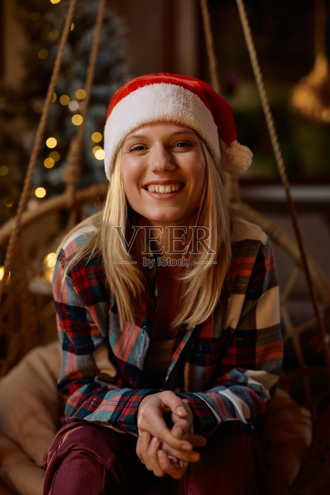 戴着圣诞帽的快乐女子在家中看向镜头。照片摄影图片