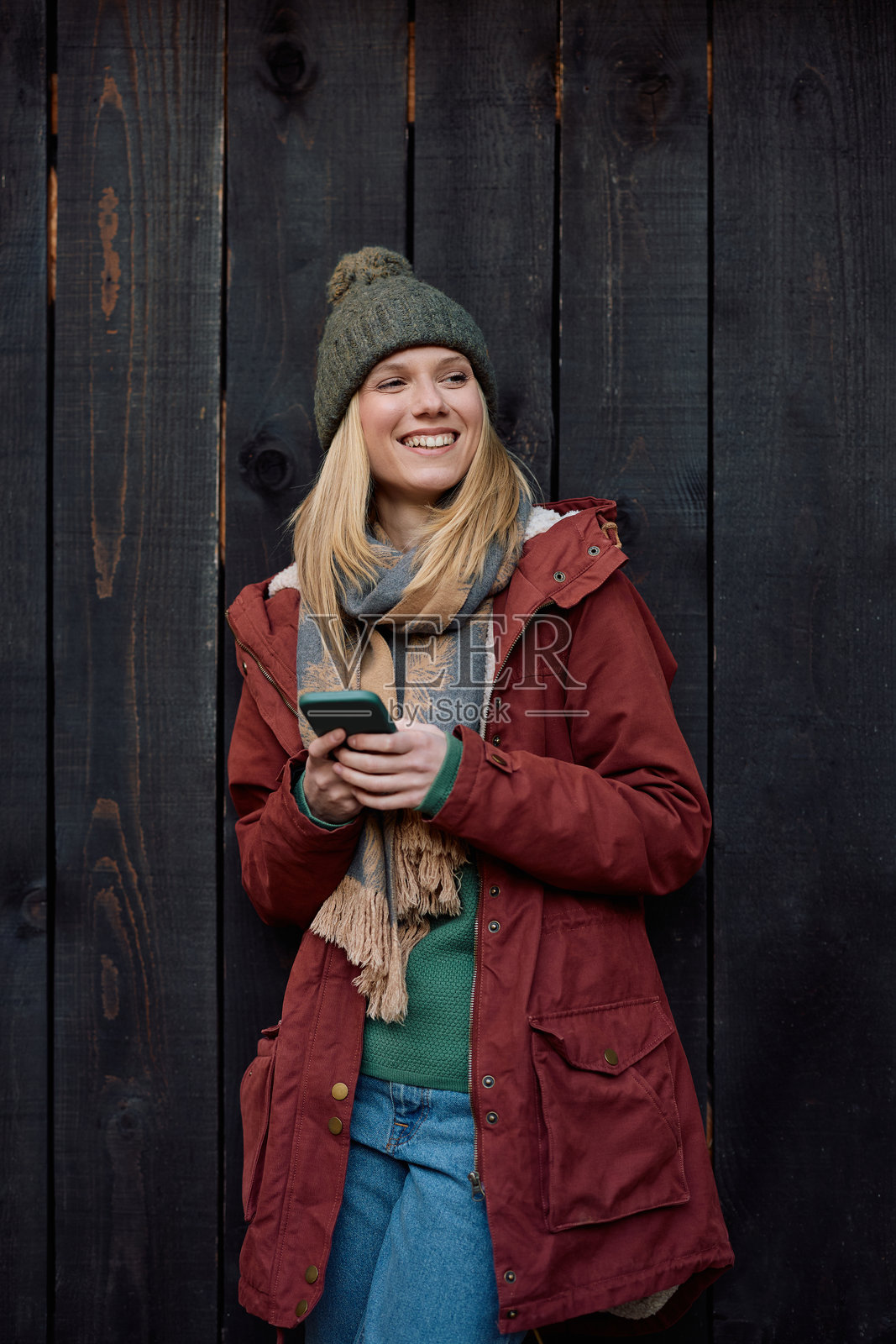 秋天,一名快乐的女子靠着木墙,正在使用手机。照片摄影图片