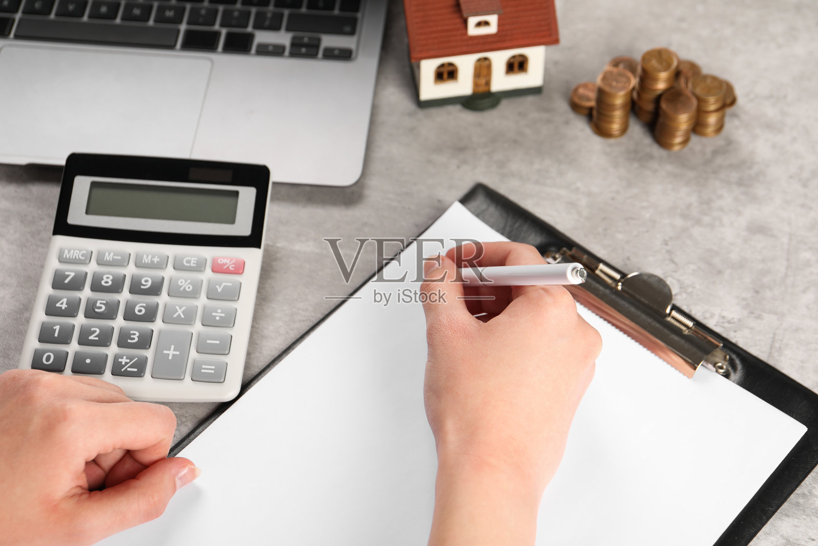 女性近景规划预算,桌上放着房屋模型、计算器和硬币照片摄影图片