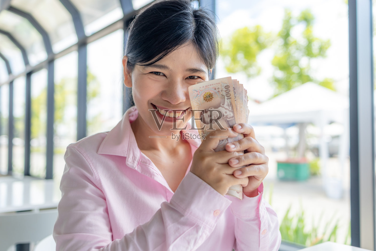 自信的亚洲女性手持泰铢纸币,象征财富、现金、富裕、财务稳定、收入增长和个人成功照片摄影图片