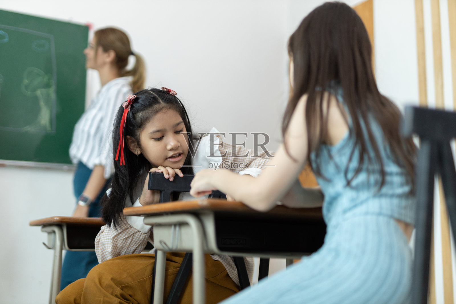 女老师在教室里教女孩们。孩子们在教室里接受教育。小学生女孩快乐学习。按照老师的指示写作。开学季的概念。照片摄影图片