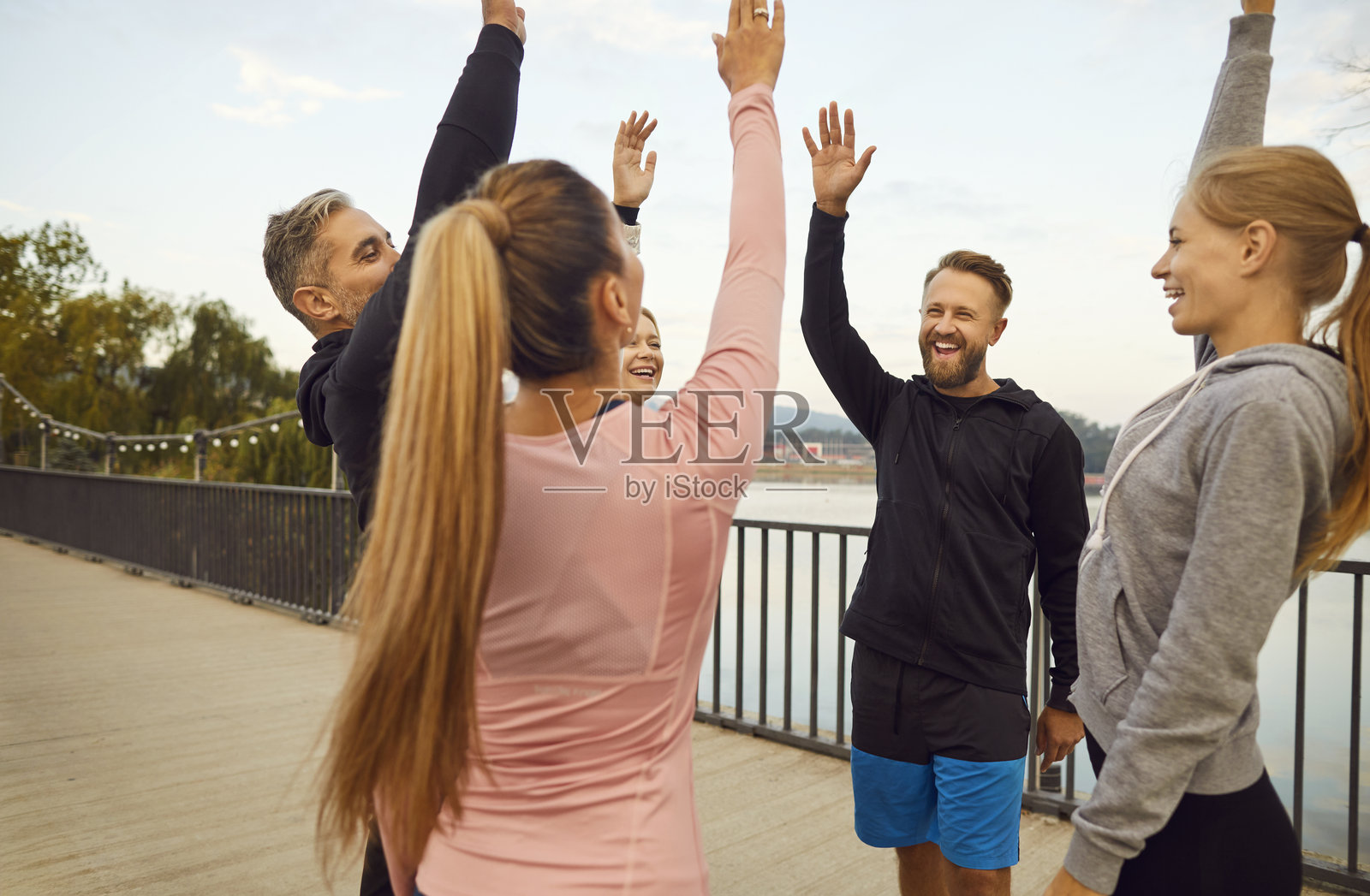 一群快乐的年轻运动爱好者在自然环境中,手举过头顶,围成一圈跳跃站立。照片摄影图片