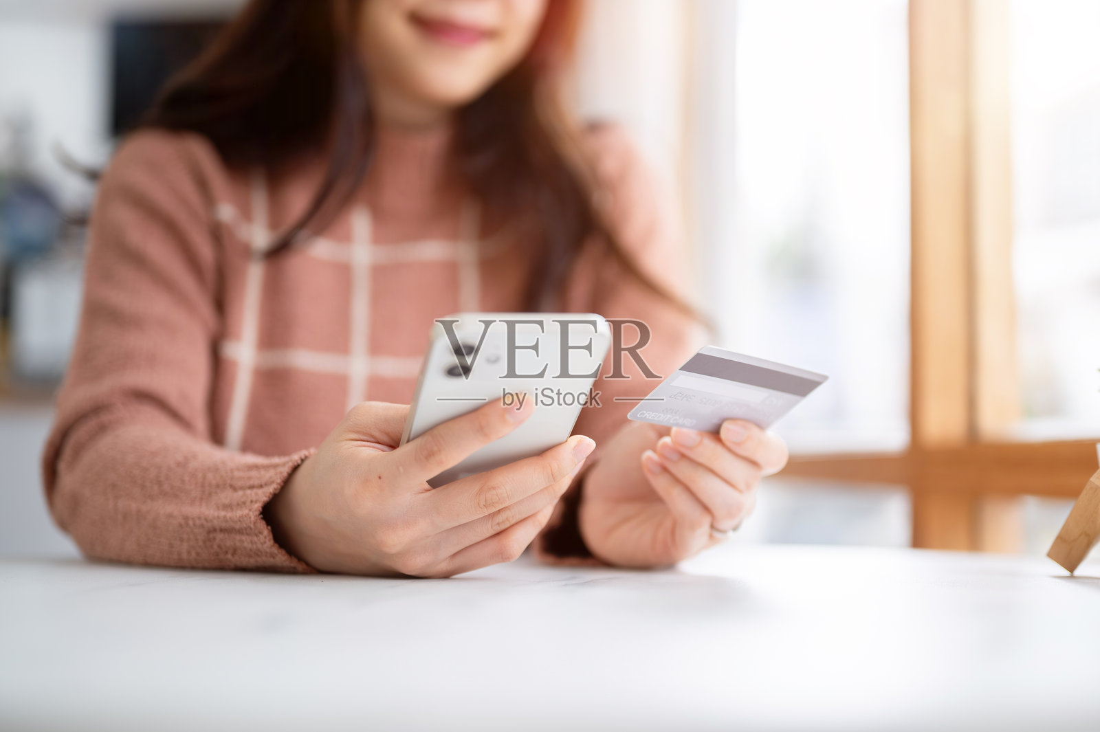 咖啡馆的玻璃墙旁,女子近距离看着手中拿着的手机,桌上放着信用卡。照片摄影图片