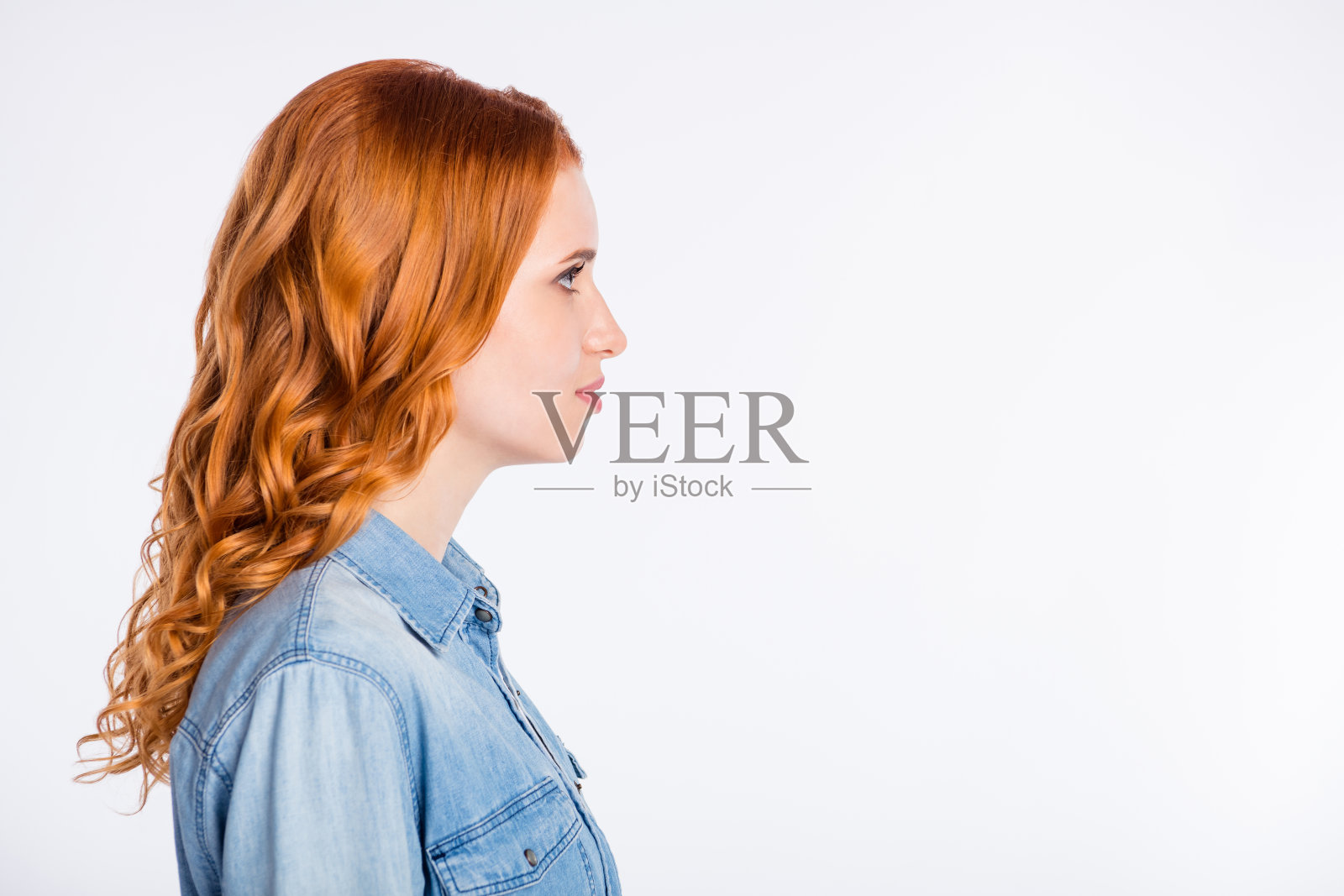 身穿红色衣服的年轻女子侧面照,表情严肃,看向空白处,背景为灰色照片摄影图片