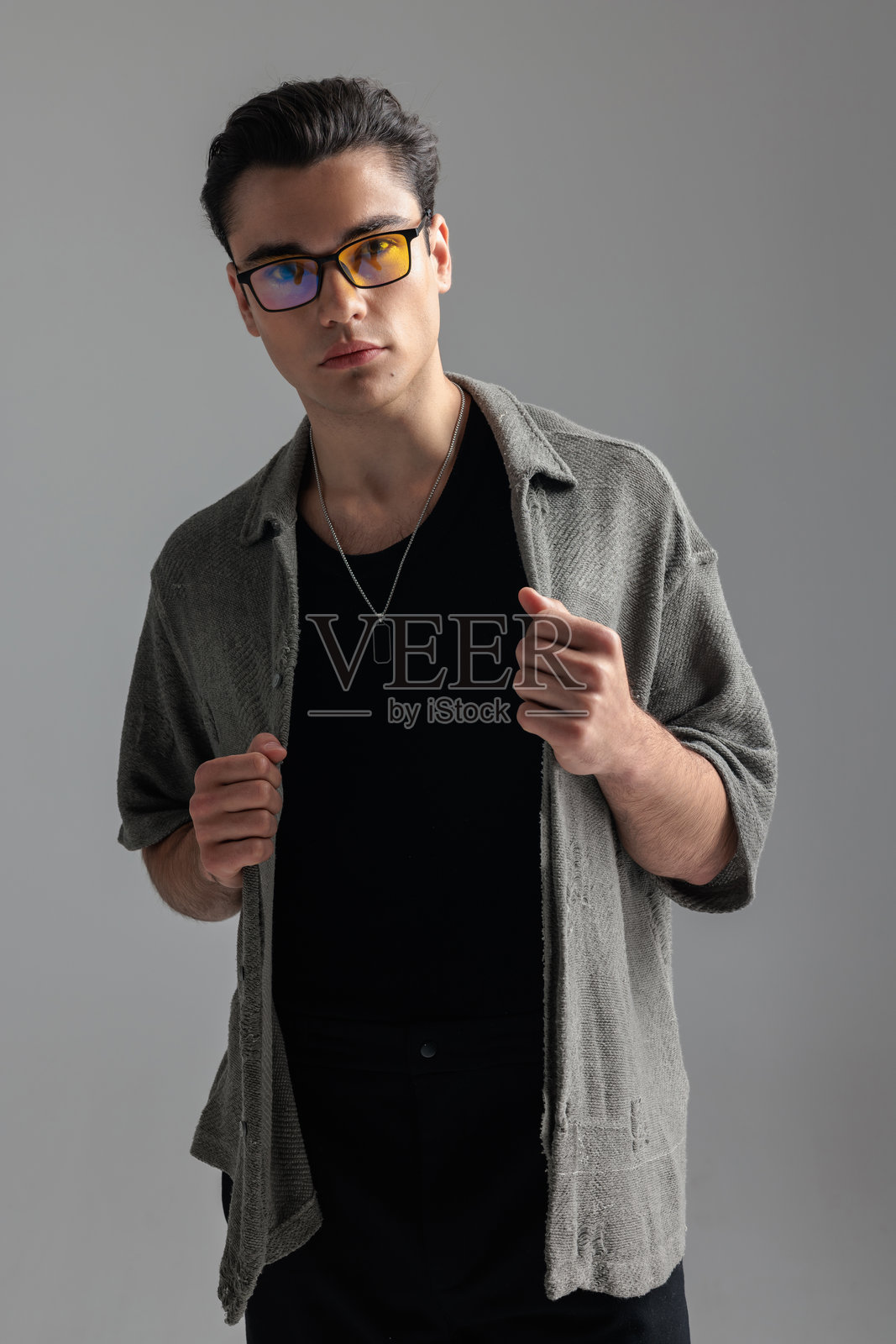 一位戴眼镜、穿着灰色开衫的英俊休闲男子正在整理衣服站着照片摄影图片