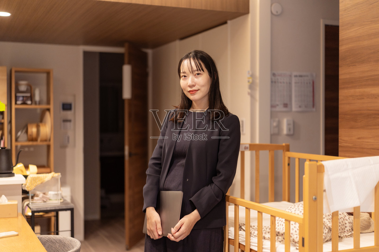 客厅里,一位职业母亲抱着笔记本电脑,婴儿在婴儿床里熟睡照片摄影图片