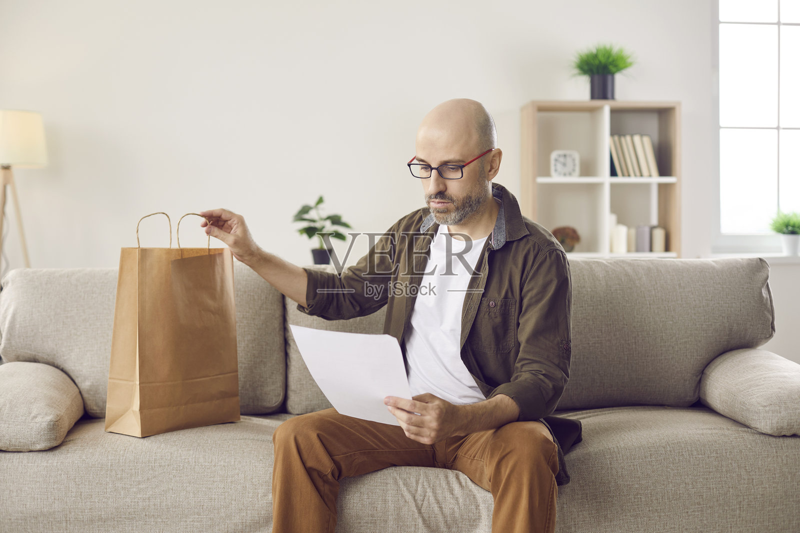 男人在家坐在沙发上,看着收到的信件和送货袋照片摄影图片