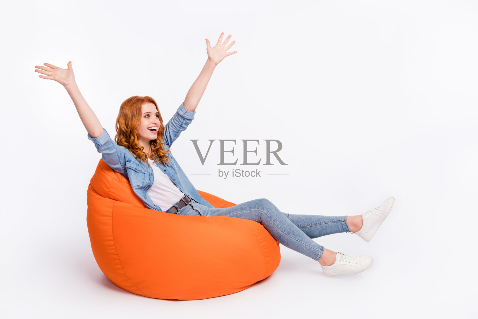 躺在豆袋椅上,年轻女孩伸展身体,露出空洞的表情,仿佛在嘲笑一位缺席的朋友,背景为纯白色。照片摄影图片