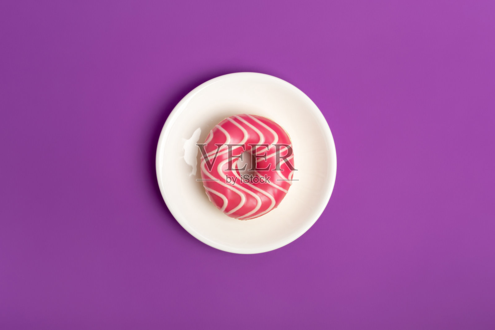 白色圆形盘子上的美味粉色糖霜草莓甜甜圈。照片摄影图片