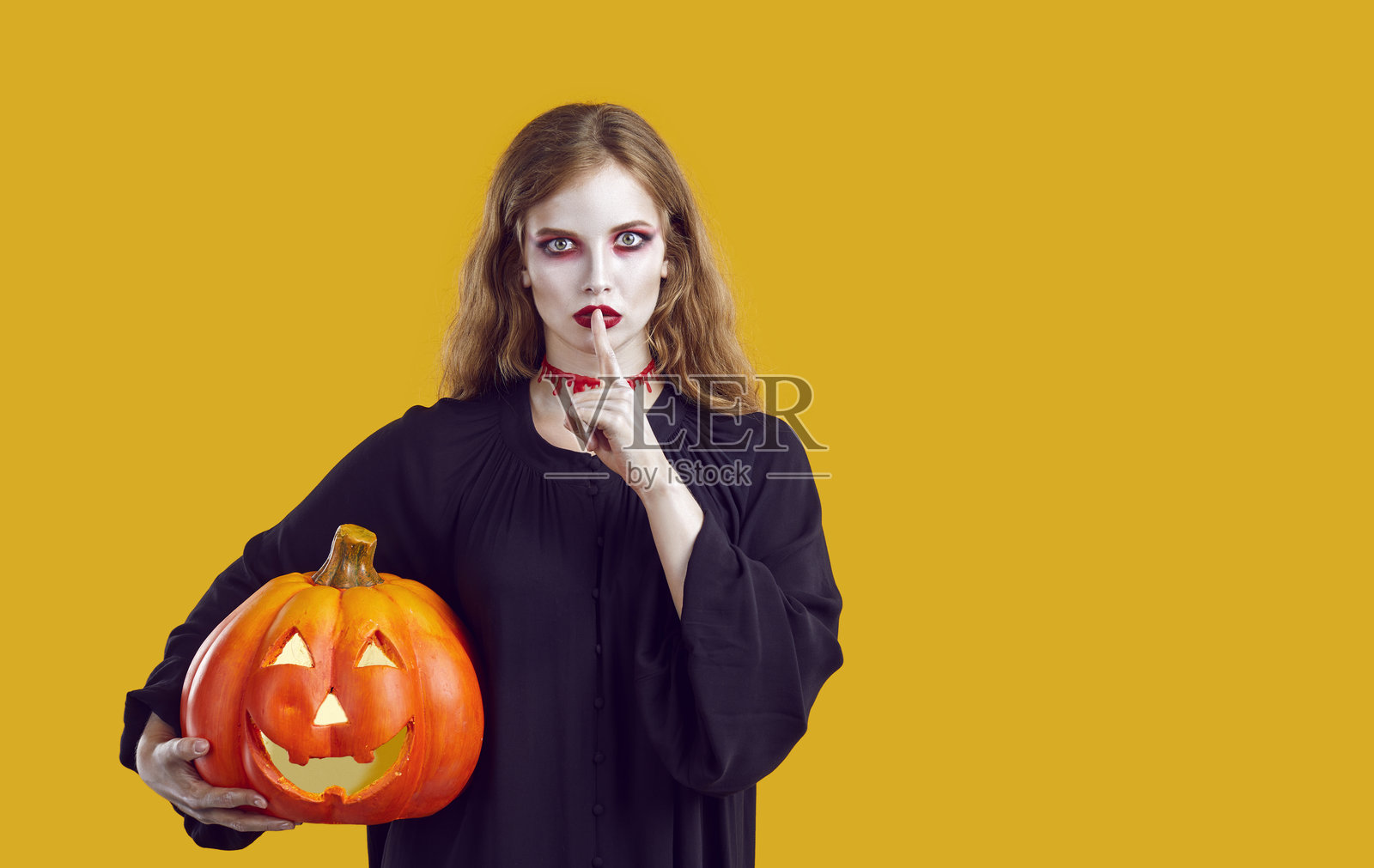 一位化着万圣节小丑妆的迷人女子,手持弯月形南瓜,并做出噤声手势。照片摄影图片