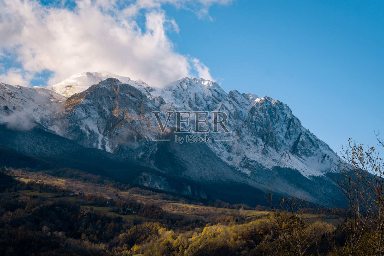 阳光下的雪山格兰萨索山,山下是秋色山谷照片摄影图片