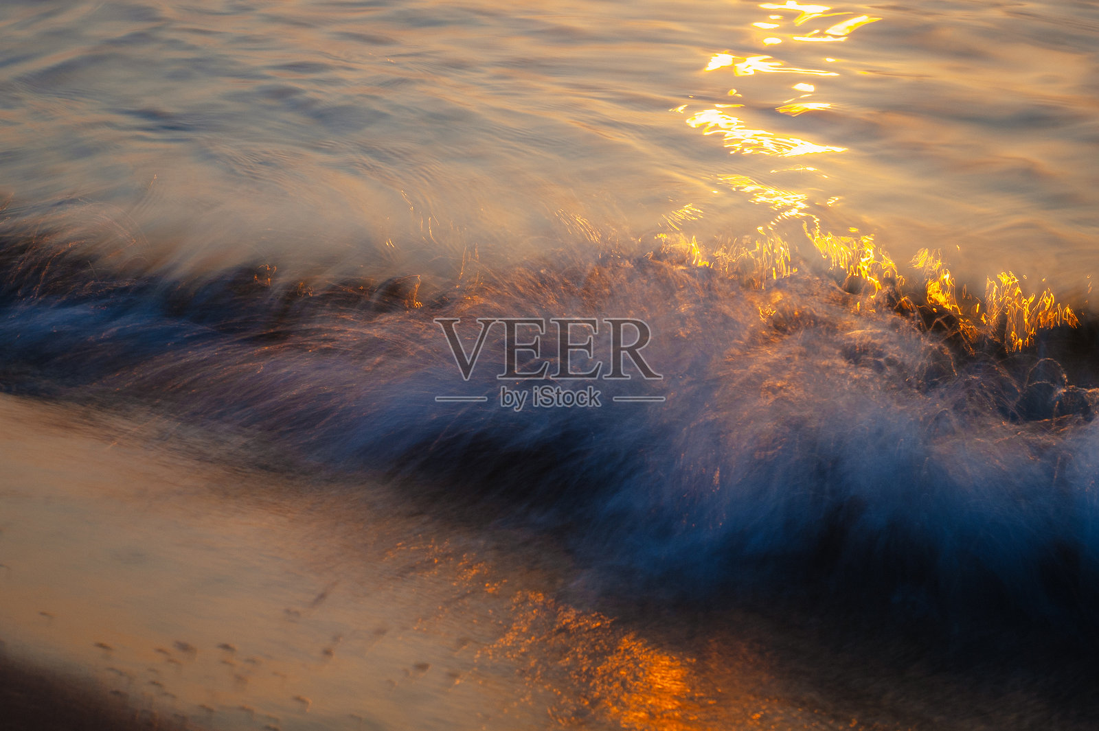 日落时分,使用长曝光技术拍摄的柔和模糊海浪拍打沙滩的景象照片摄影图片