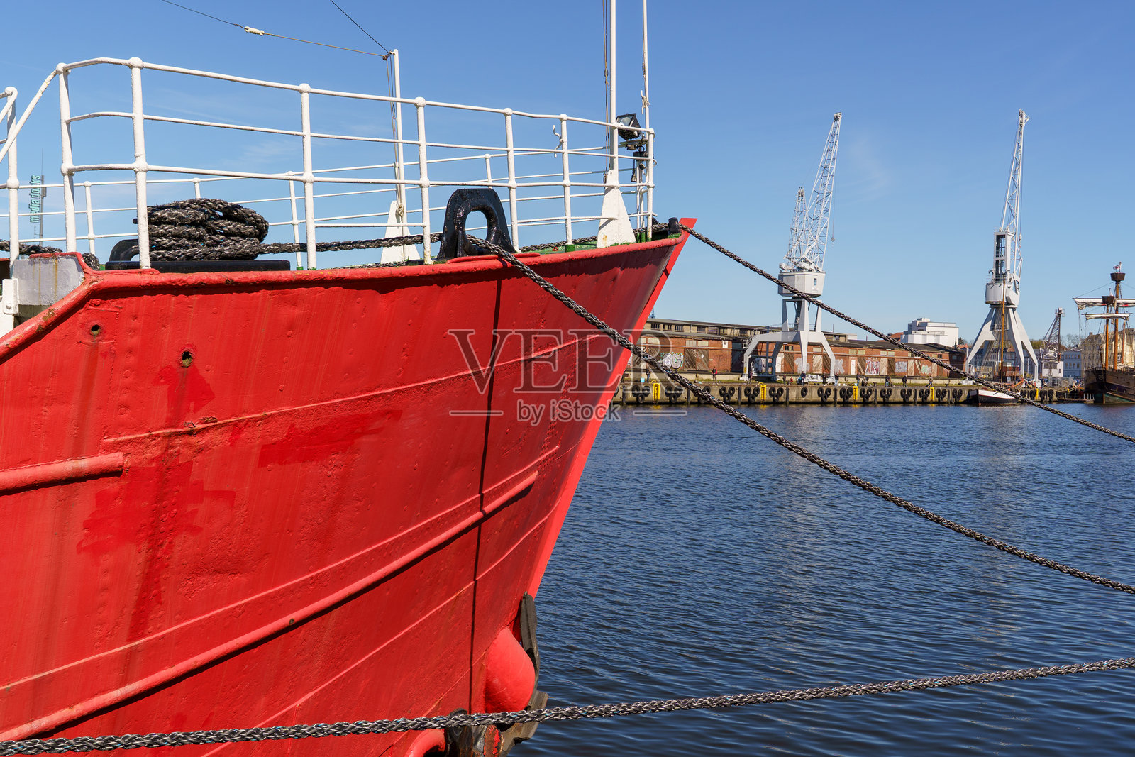 德国吕贝克市停靠的红色船只的船头,背景中可以看到港口起重机。照片摄影图片