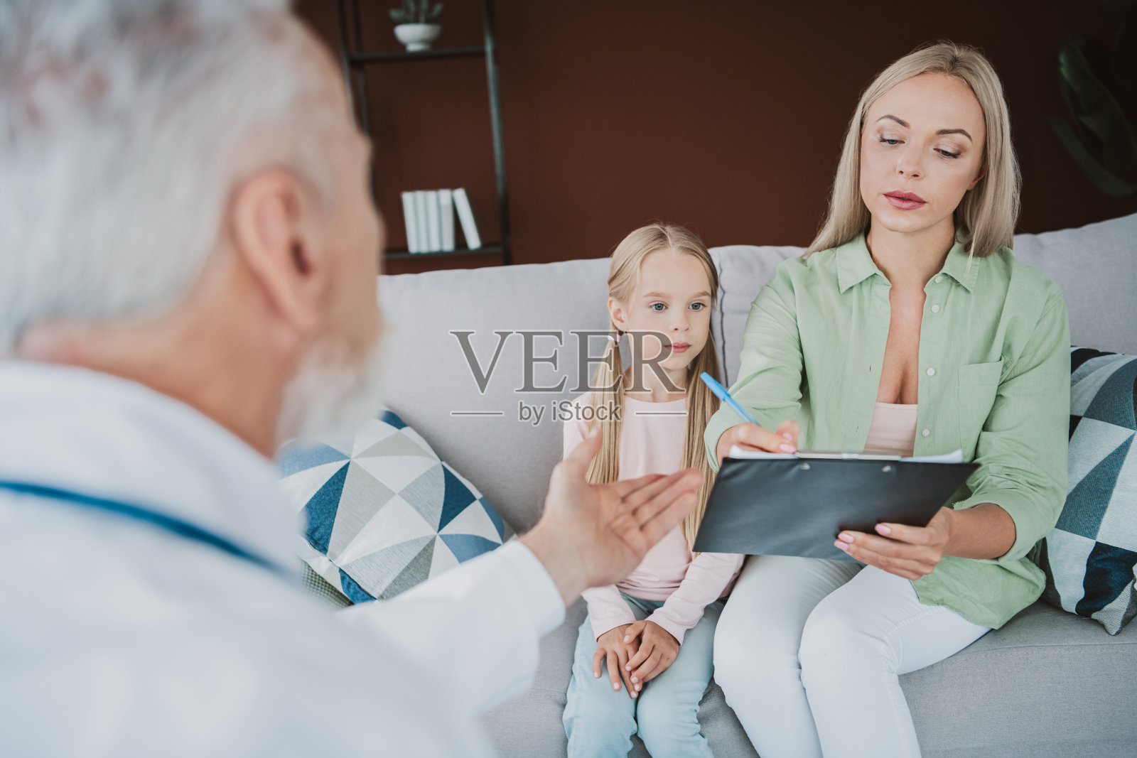 一位充满关怀的专业人士在家中舒适的客厅里,与一位母亲和她的女儿聊天,分享指导和安慰,构成了一个温馨的家庭时刻。照片摄影图片