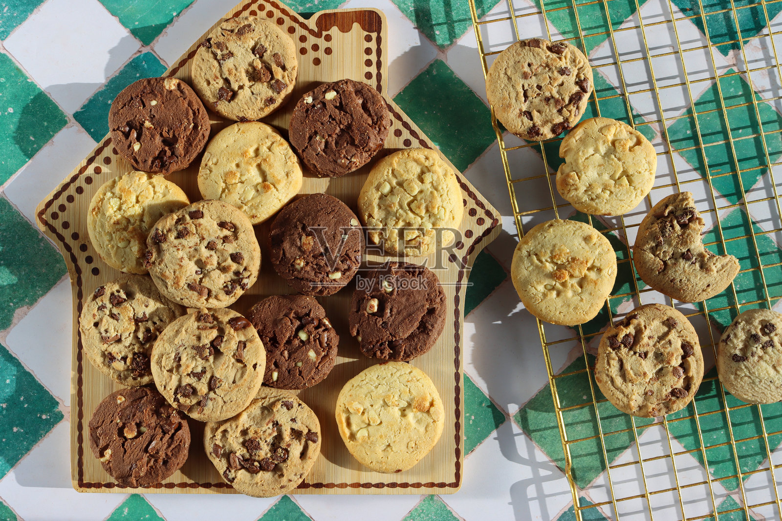 姜饼屋设计面包板和金属冷却架上的巧克力豆酥饼圆饼,节日三倍巧克力豆、牛奶巧克力豆和白巧克力豆饼干,白色和绿色格子图案背景照片摄影图片