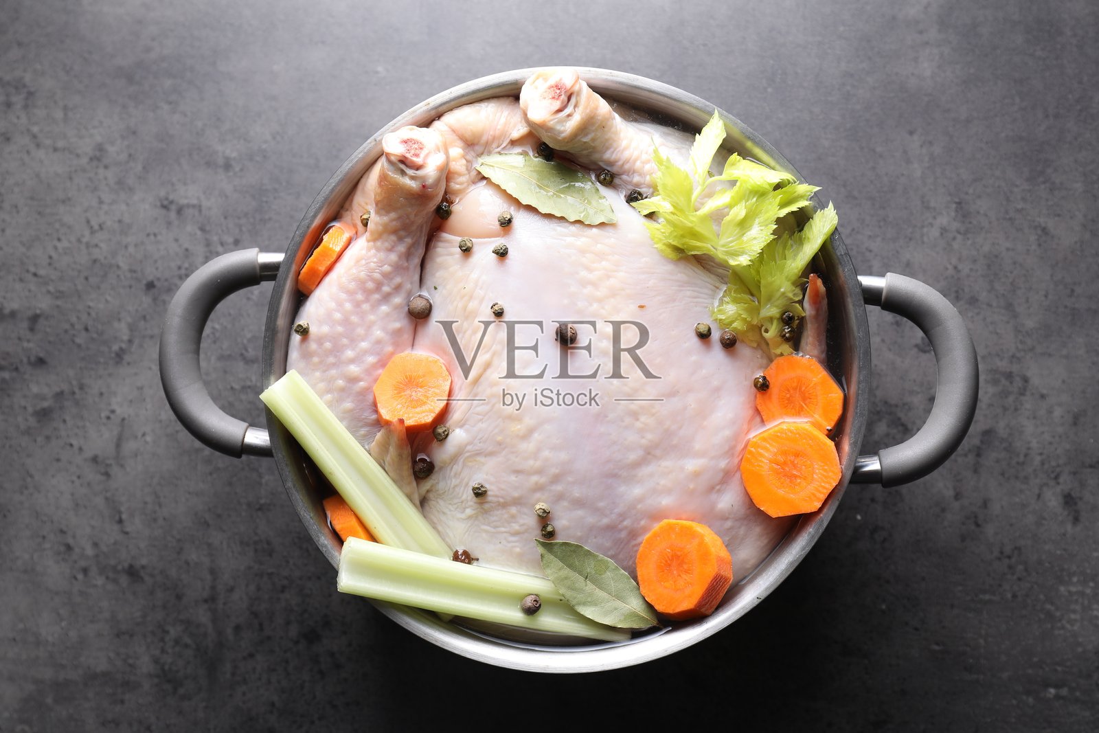 俯视角度,灰色纹理桌上的锅里装着整只生火鸡、切好的胡萝卜、芹菜和香料照片摄影图片