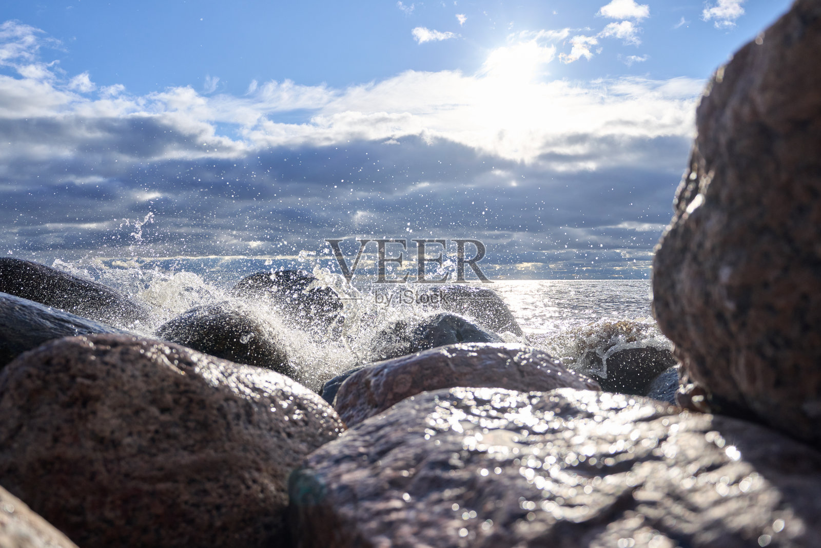 阳光映照下的海浪拍打着岩石,远方地平线云雾缭绕。照片摄影图片