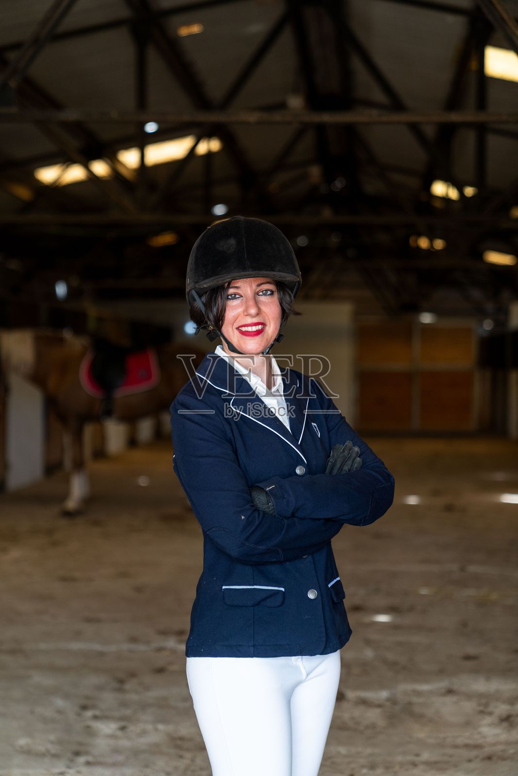一位微笑的女骑手正在马厩里与她的马合影。照片摄影图片