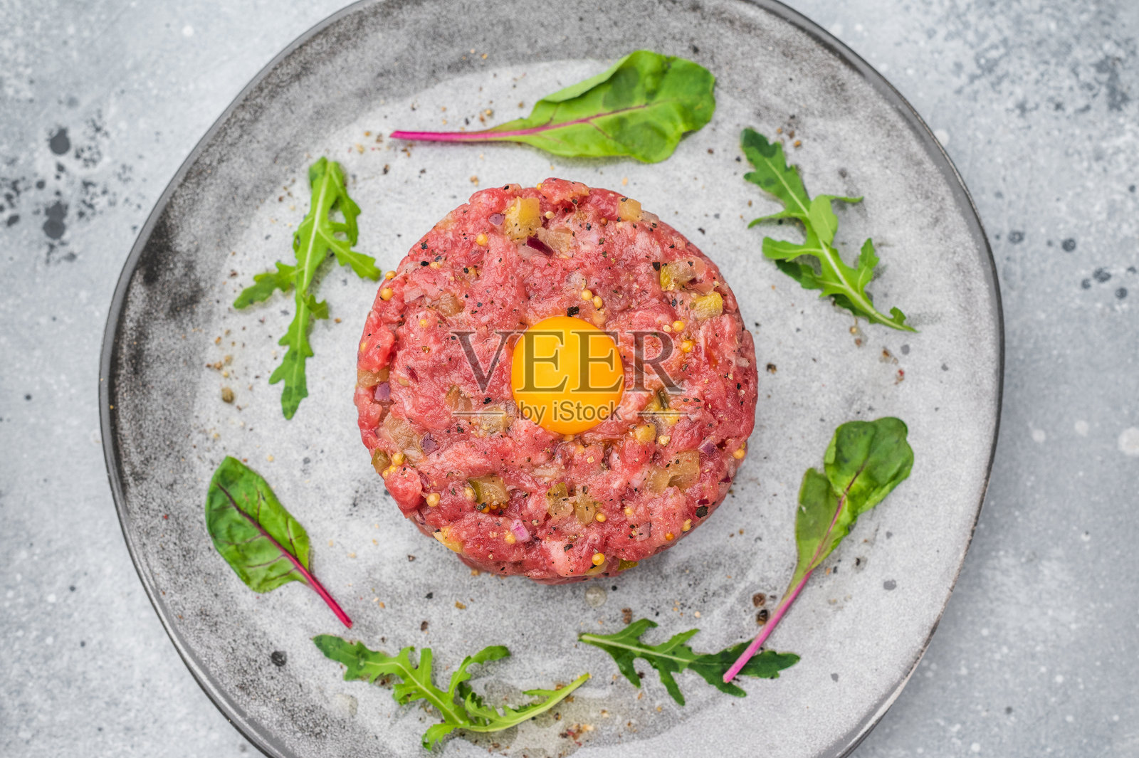 石头盘子里的生牛肉塔塔,配有蛋黄和蔬菜,背景为灰色,非常适合高蛋白餐、美食烹饪和高品质食品摄影。照片摄影图片
