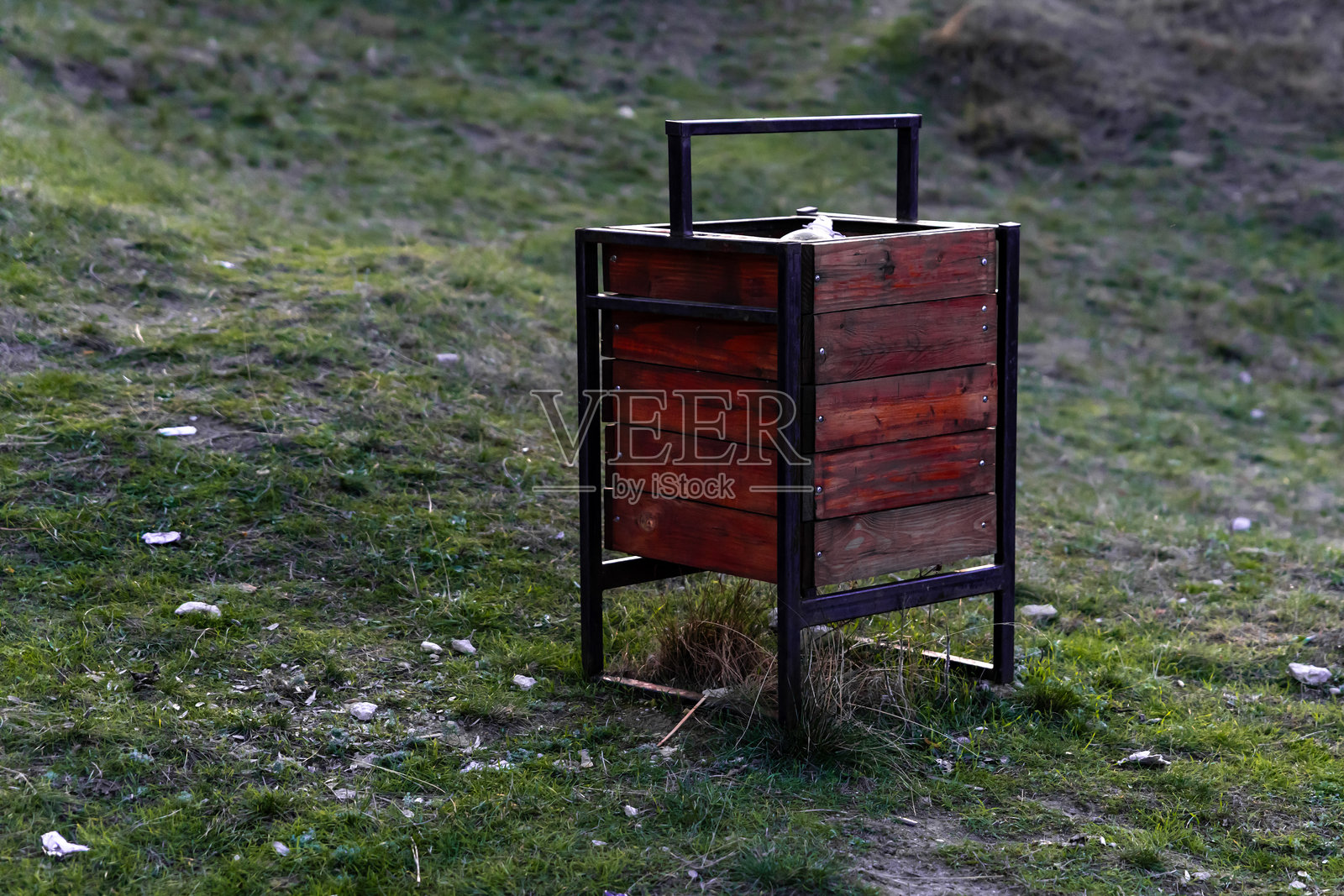 木制带金属框架的垃圾桶放置在户外的草地上,非常适合清洁、环境和公共空间等主题。照片摄影图片