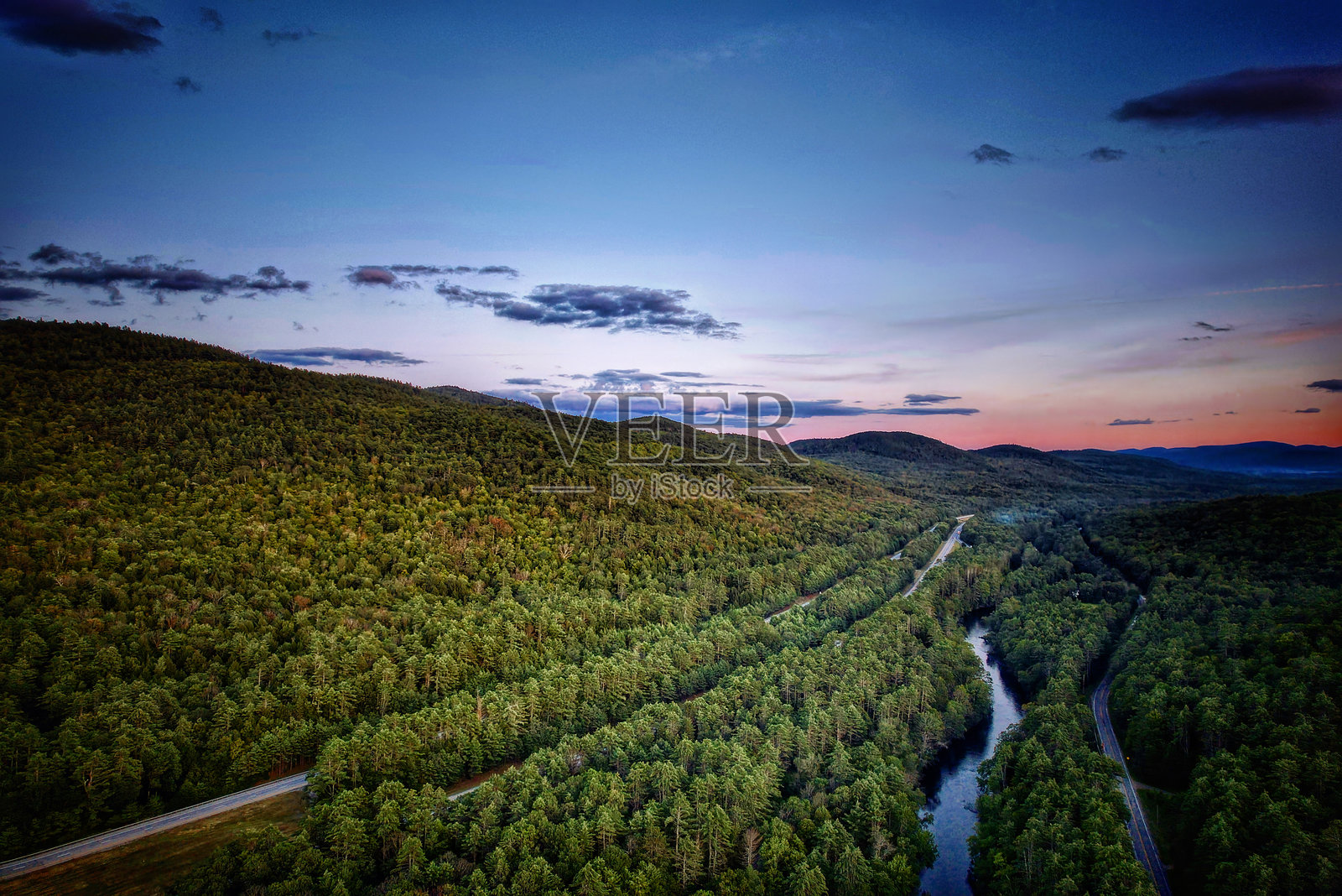 夕阳下的佛蒙特州葱郁山谷,一条河流蜿蜒穿过茂密的森林,远方是连绵起伏的山峦。照片摄影图片