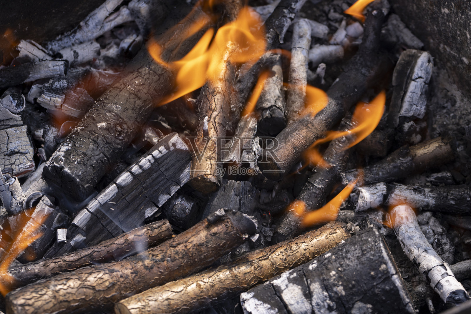 用果树木头搭起篝火,橙色的火焰在准备烧烤的肉类,烤架上燃烧的木头会产生炭火来烤肉。照片摄影图片