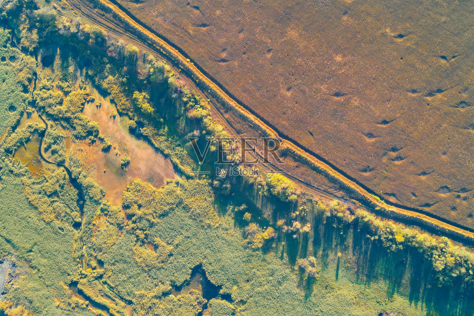 湿地边界道路抽象。航拍图显示堤坝或道路分隔着沼泽水道和秋叶覆盖的棕色干田。照片摄影图片