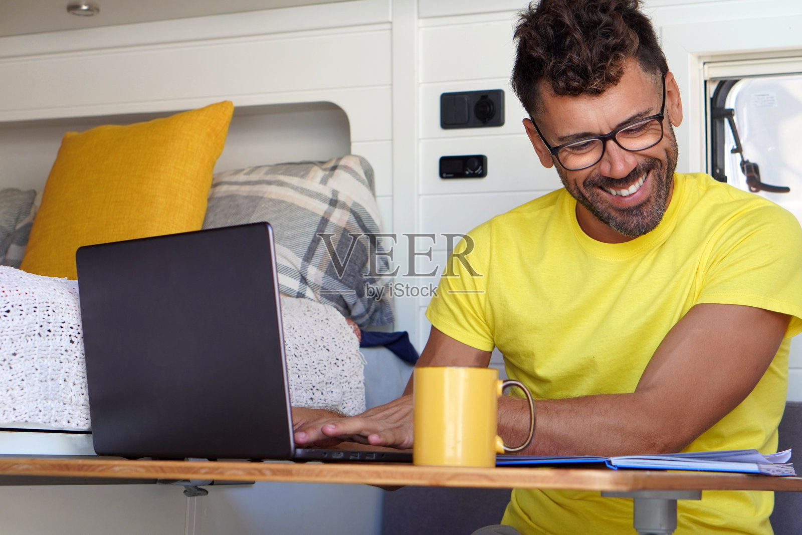 数字游民、旅行和远程工作。一个穿着黄色T恤的男人正在他的露营车里工作。照片摄影图片