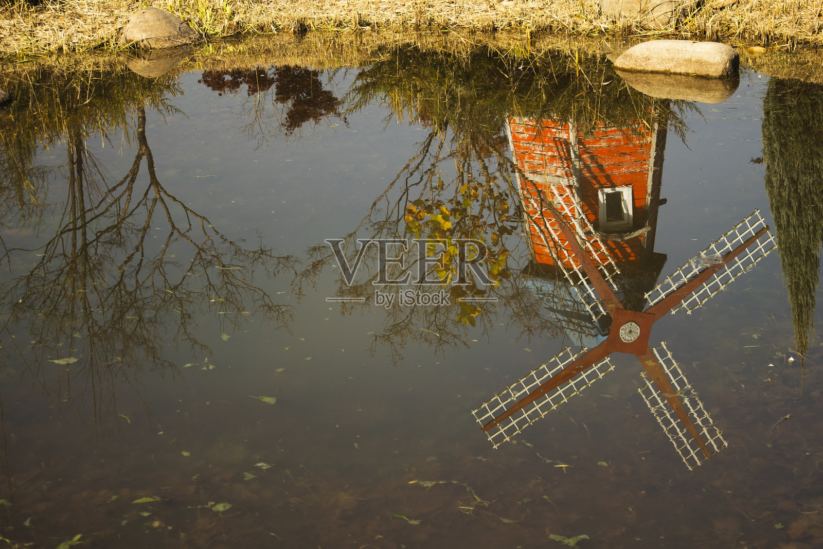 宁静的秋日池塘中倒映着风车和树木。照片摄影图片