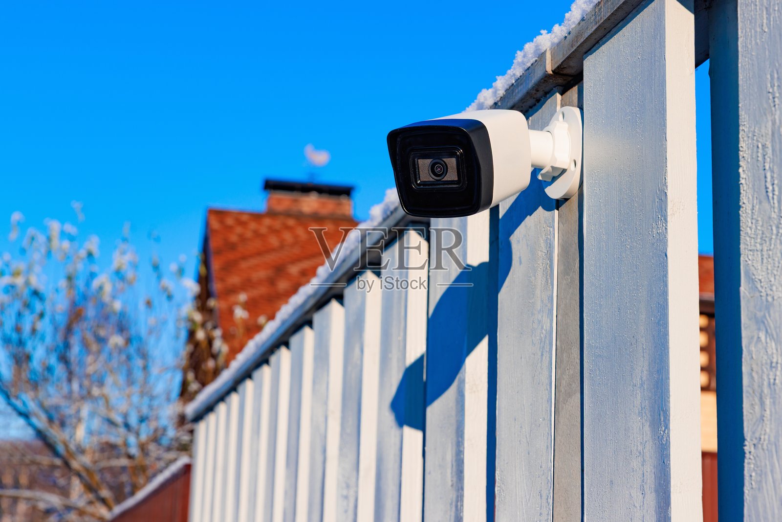 安装在木质栅栏上的户外监控摄像头,背景是晴朗的冬季天空,地面有少量积雪照片摄影图片