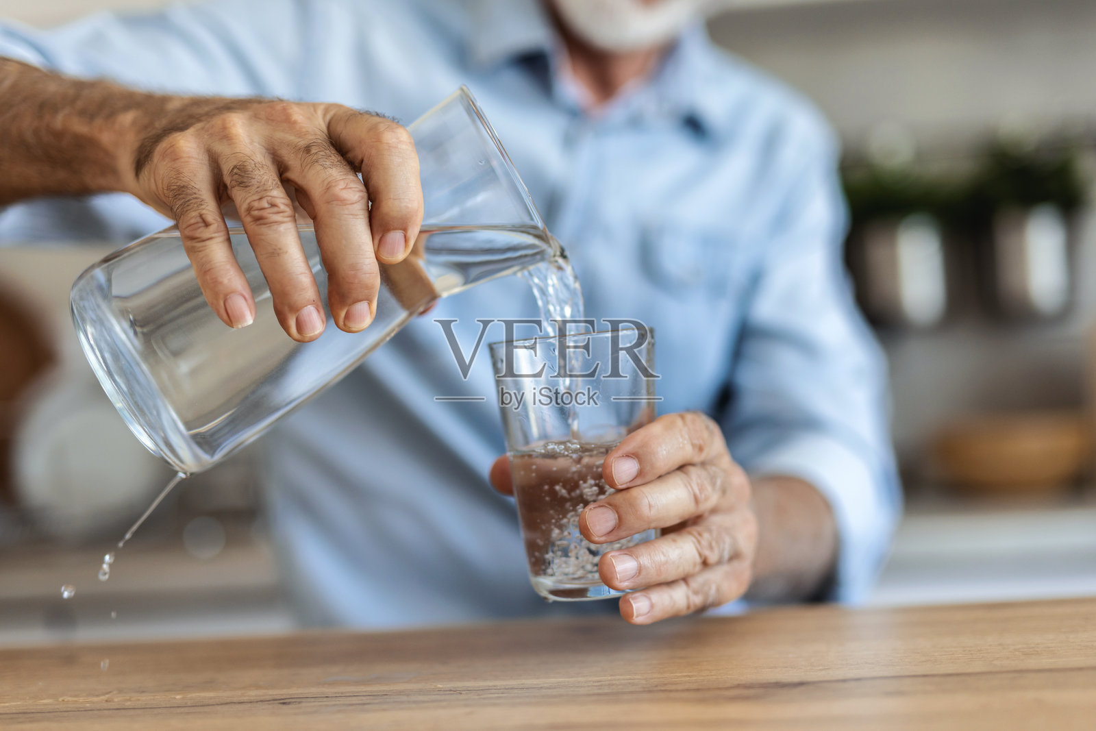 一位长者在厨房里喝水以补充水分,并沉思过去的生活。这位老人手中拿着玻璃杯,饮用清爽的饮料,思绪万千,回忆着往昔,展望着未来的健康。照片摄影图片