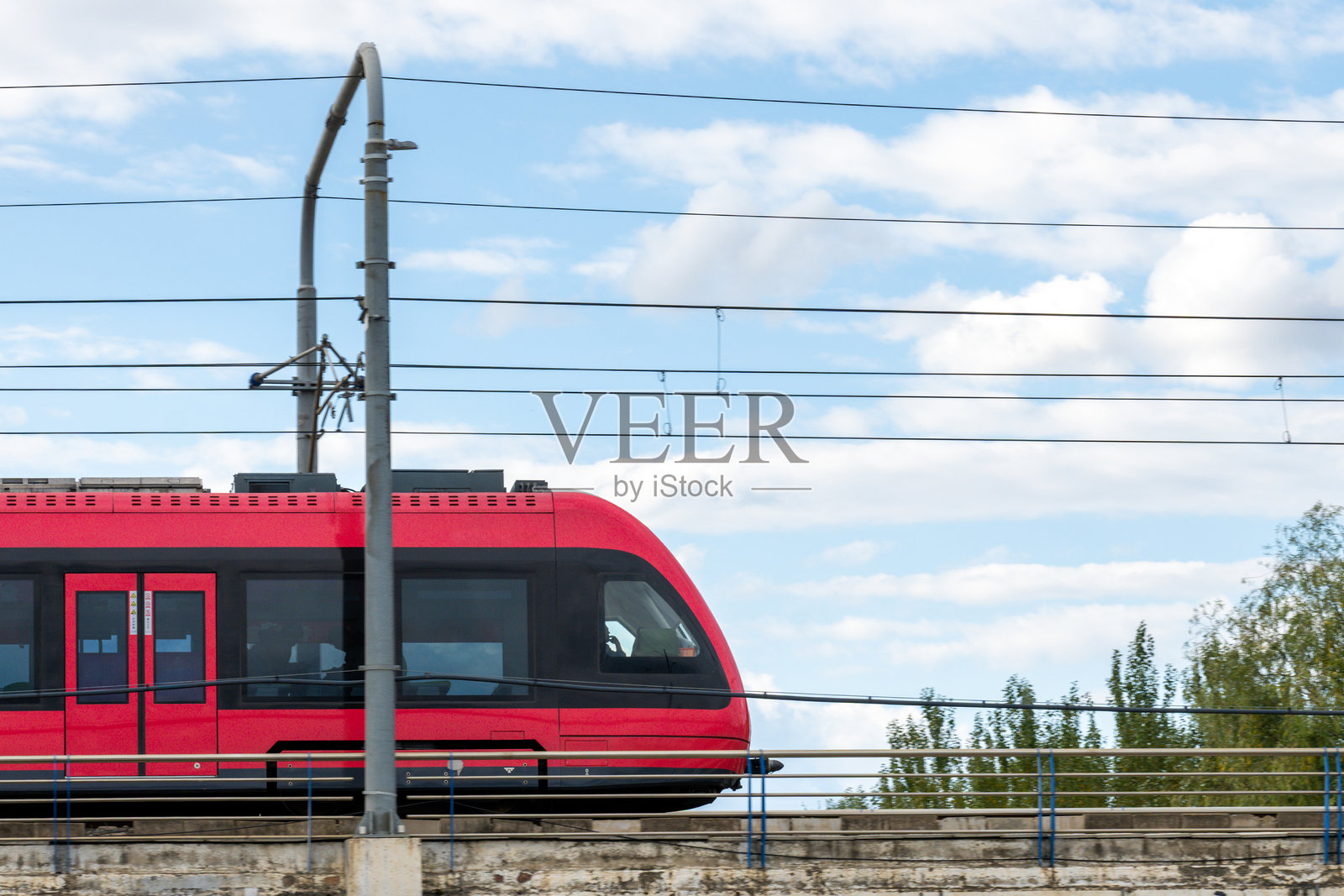 一辆红色的现代电动火车在蓝天白云下的城市轨道上行驶照片摄影图片