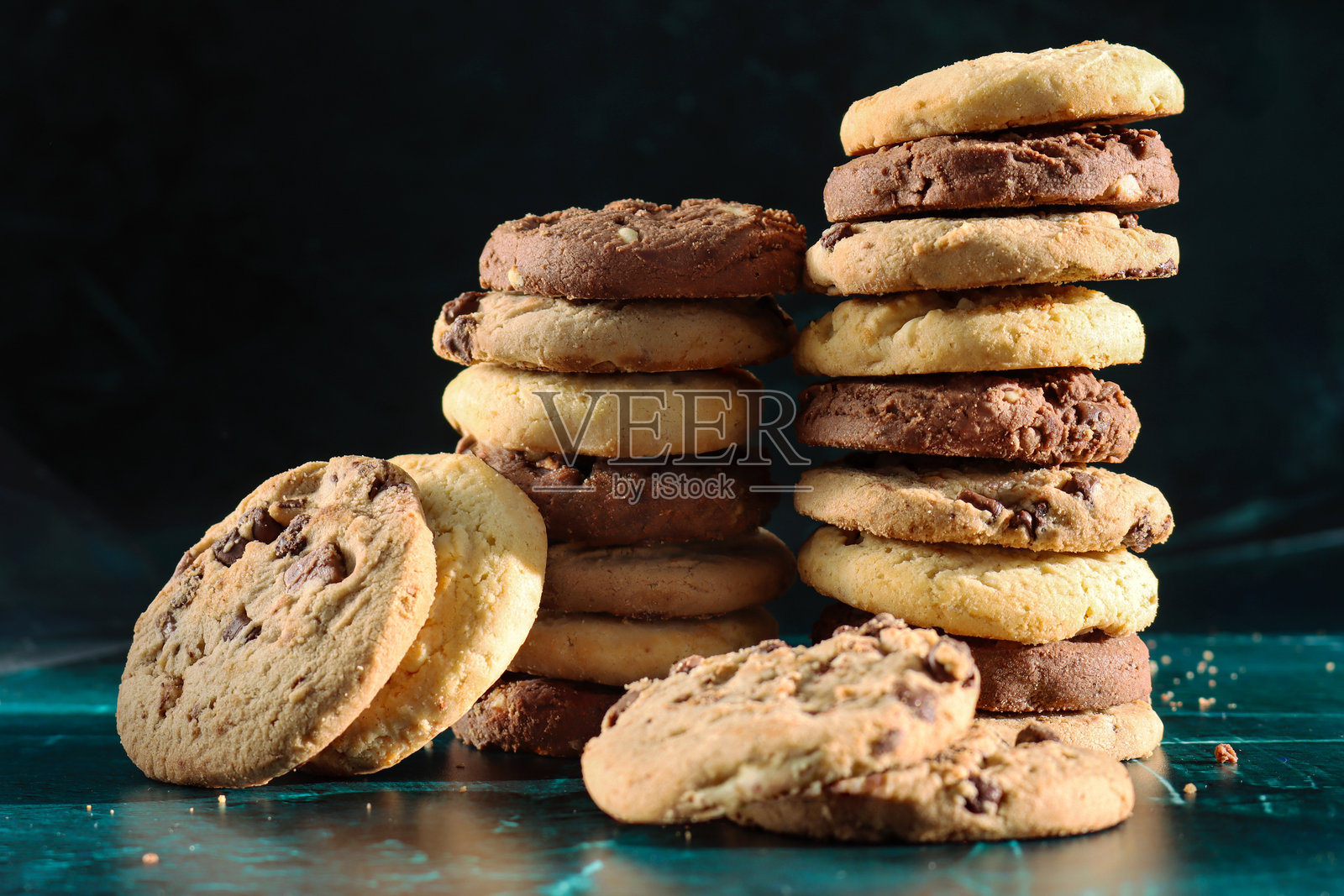 巧克力碎饼干堆叠在不同巧克力碎的酥饼周围,有三层巧克力碎、牛奶巧克力碎和白巧克力碎的饼干,表面有斑驳的绿色,背景为黑色,焦点在前景。照片摄影图片