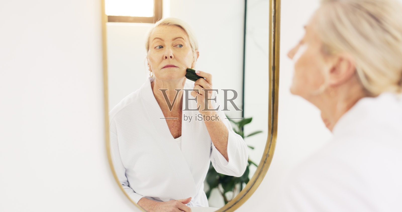 老年女性在浴室镜子前使用刮痧和护肤工具,促进家中血液循环和美容。老年人,抗衰老,反映出血液流动、按摩和退休之家的皮肤病学。照片摄影图片