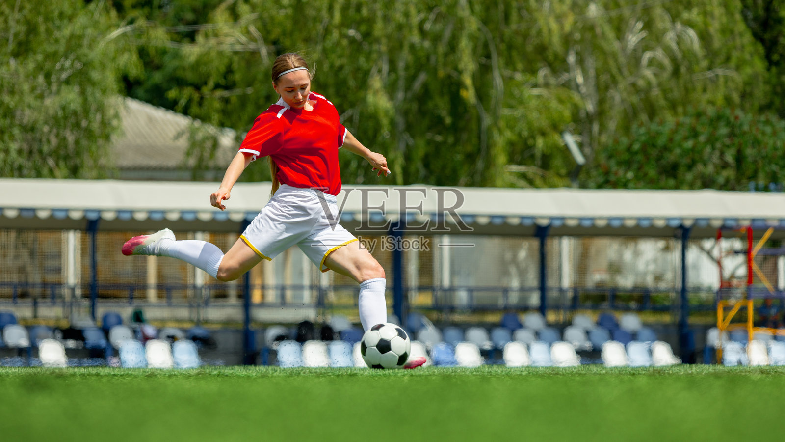 身穿红色球衣的女性足球运动员在绿色球场上踢足球照片摄影图片