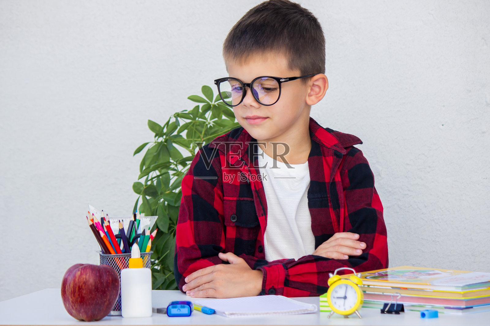 戴眼镜的聪明小男孩准备上学,正在从书桌上的收纳盒里挑选铅笔。照片摄影图片